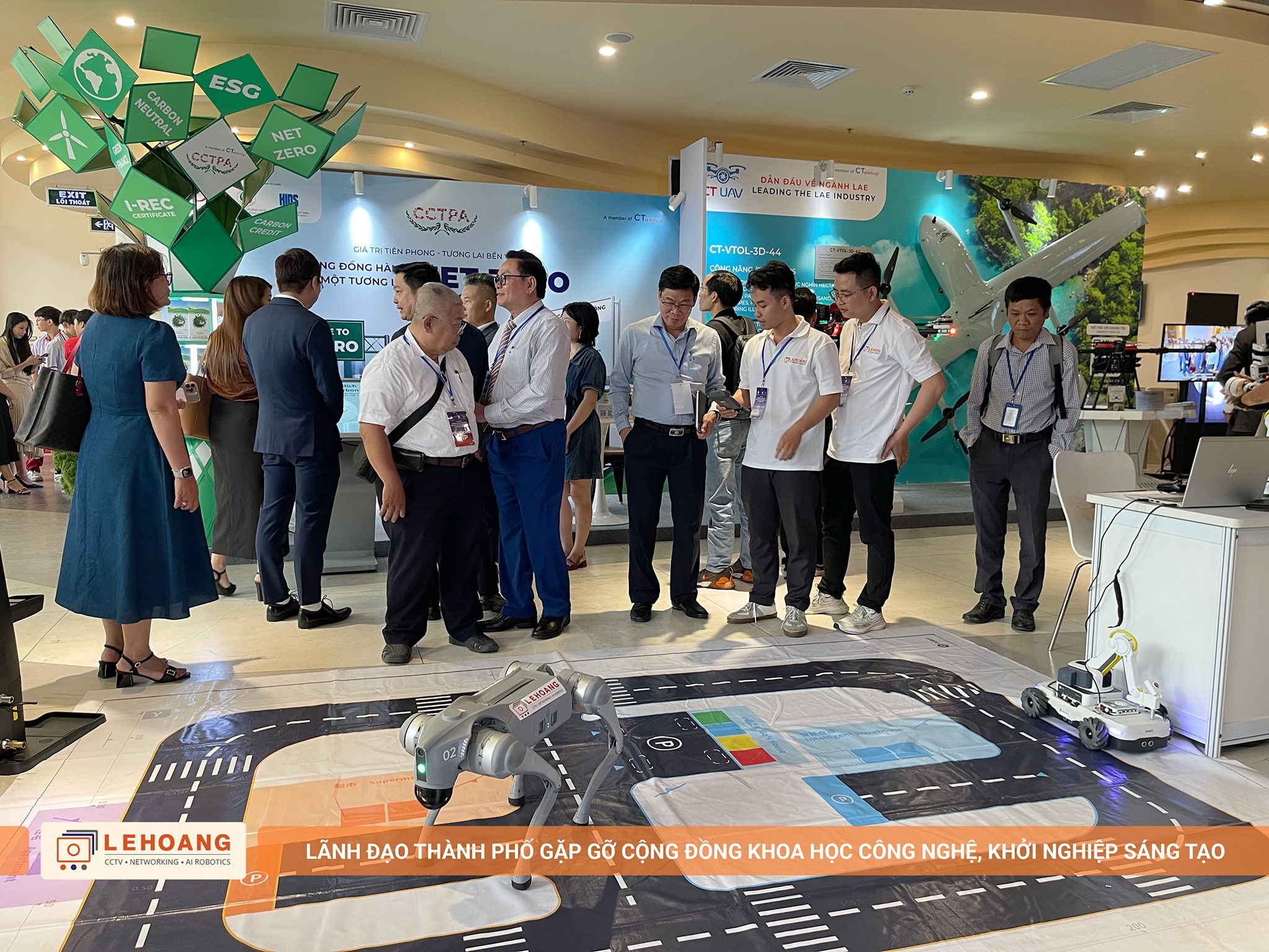 Đoàn lãnh đạo và khách tham quan dừng chân tại gian hàng Lê Hoàng Robotics, robot chó Unitree Go2 trình diễn trên thảm mô phỏng đường phố, bên cạnh là robot vệ sinh Gausium Phantas