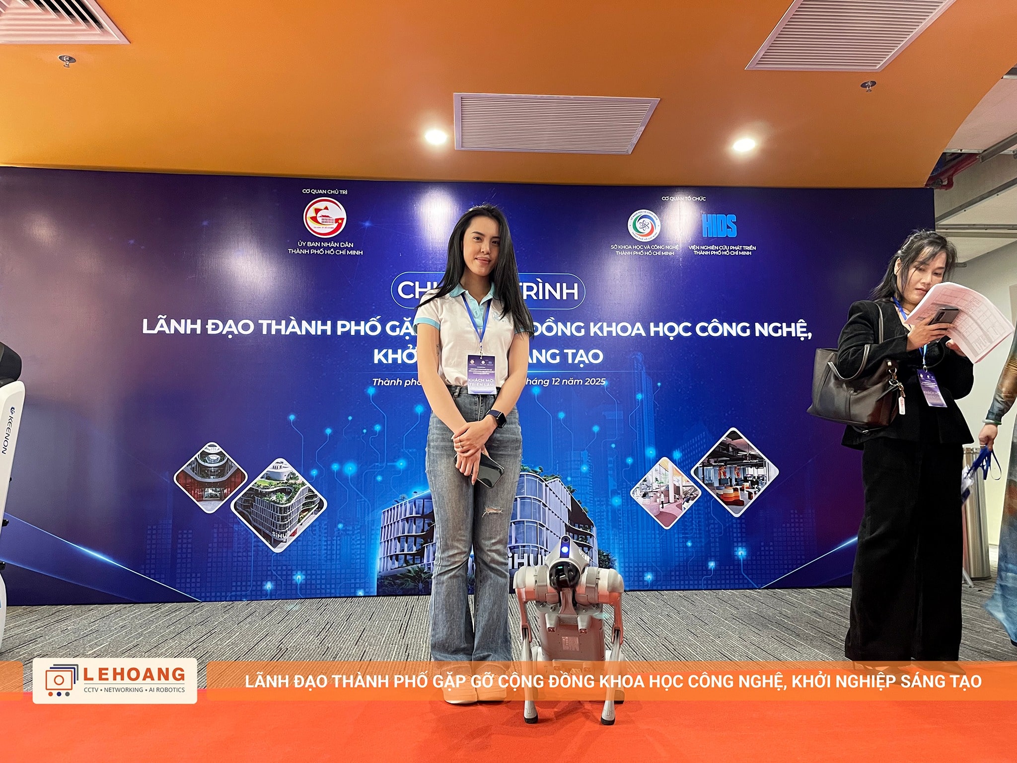 Nhân viên Lê Hoàng Robotics chụp ảnh cùng robot chó Unitree Go2 trước backdrop chính thức của chương trình 