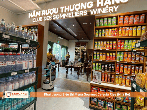  Robot phục vụ KEENON di chuyển trong khu vực Hầm Rượu Thượng Hạng - Club Des Sommeliers Winery tại siêu thị Mena Gourmet Celesta Rise, bên cạnh các kệ trưng bày rượu vang, nước giải khát và bánh snack cao cấp.